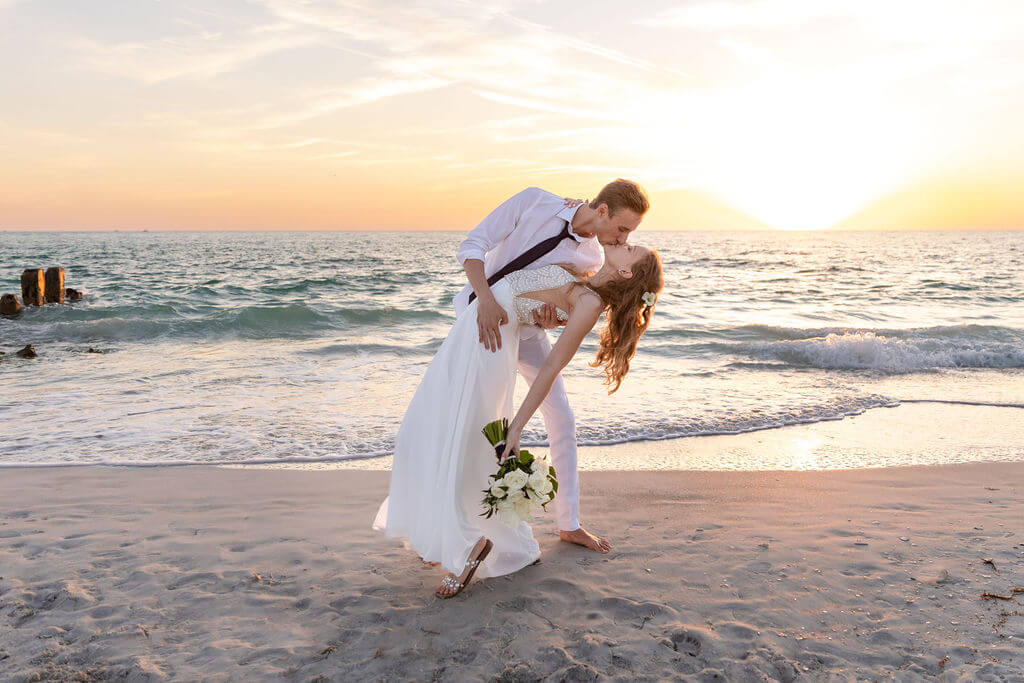 A newlywed couple sharing a dip and a kiss at sunset on a Gulf Coast beach — a real Dream Beach Weddings ceremony
