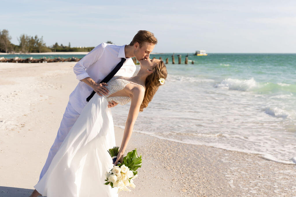 A newlywed couple sharing a dip and a kiss at sunset on a Gulf Coast beach — a real Dream Beach Weddings ceremony