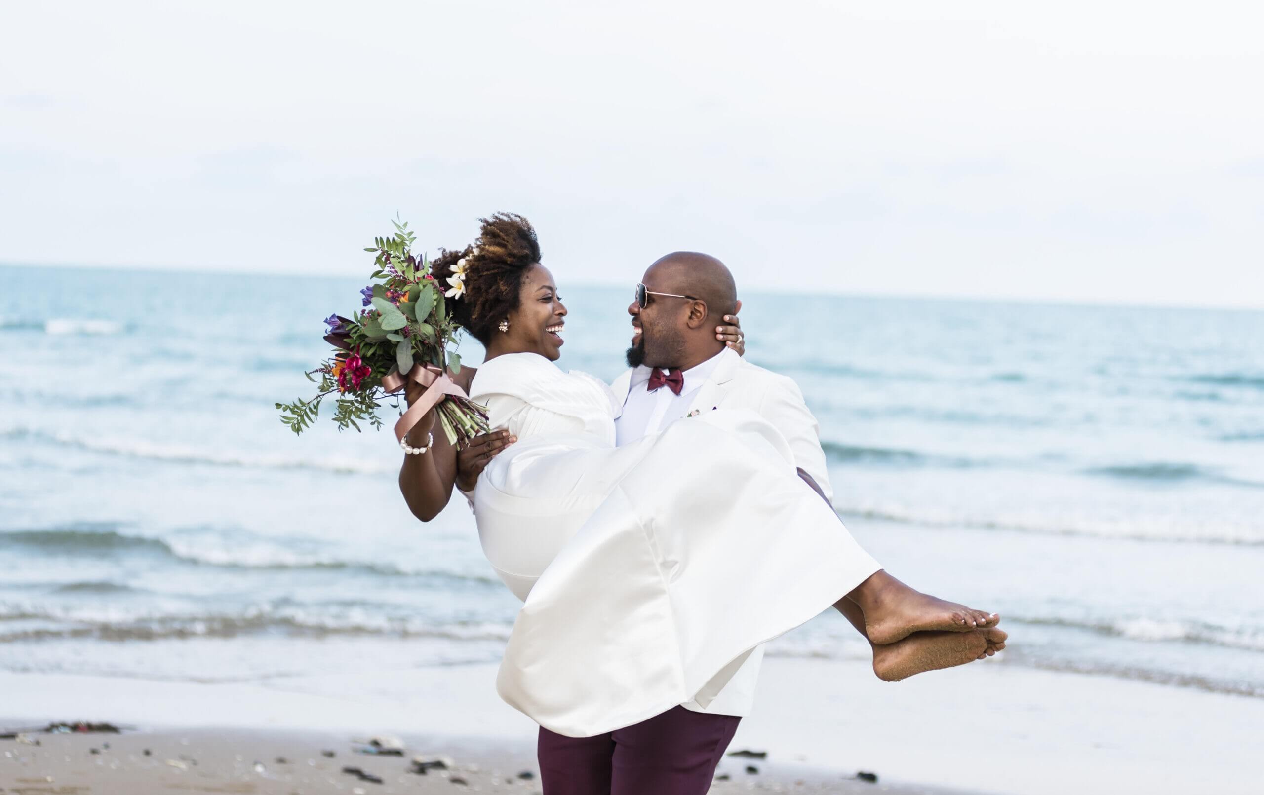 Groom carrying his laughing bride with a colorful bouquet at Bradenton Beach