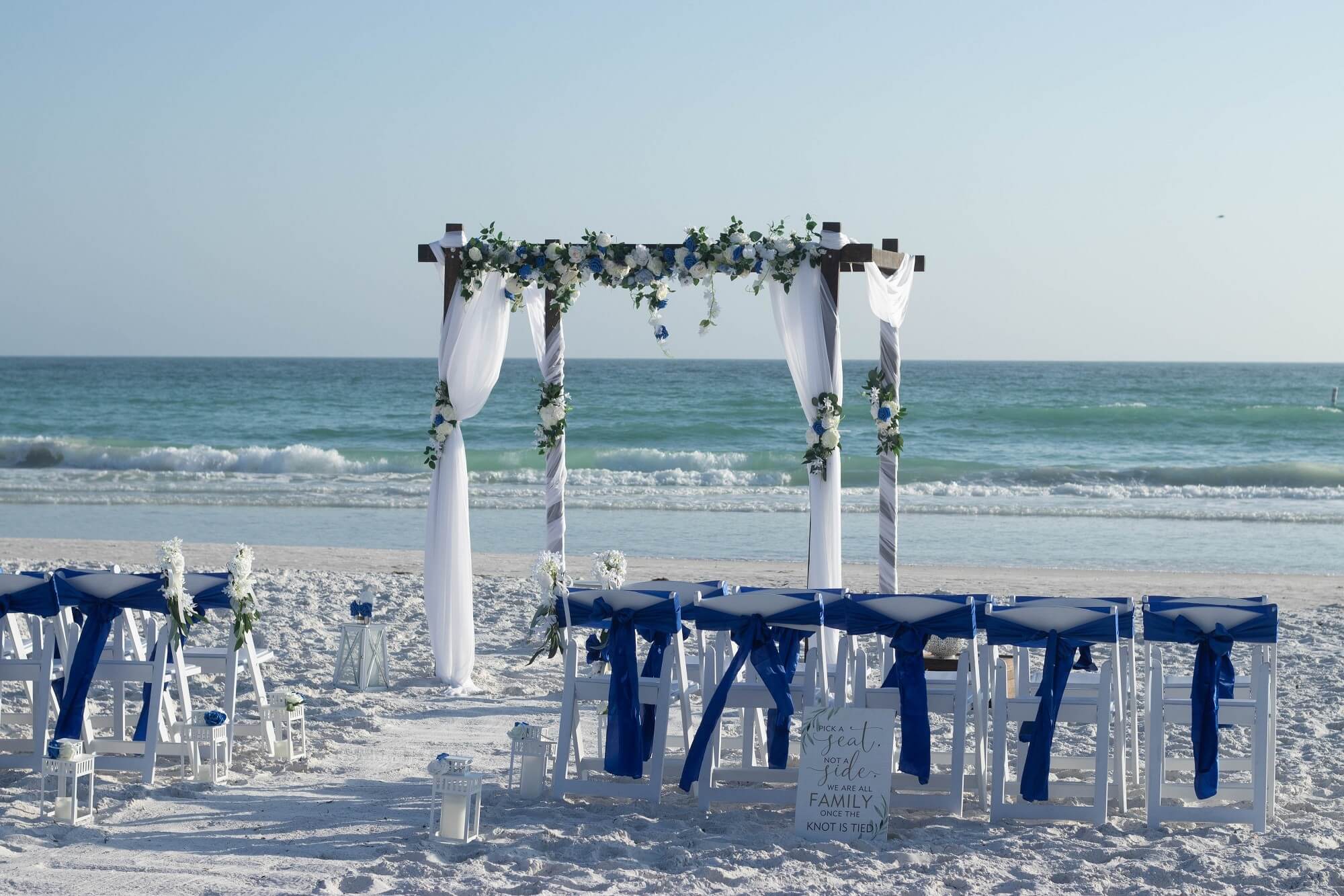 Blue-and-white floral arch with royal-blue chair sashes on Lido Beach