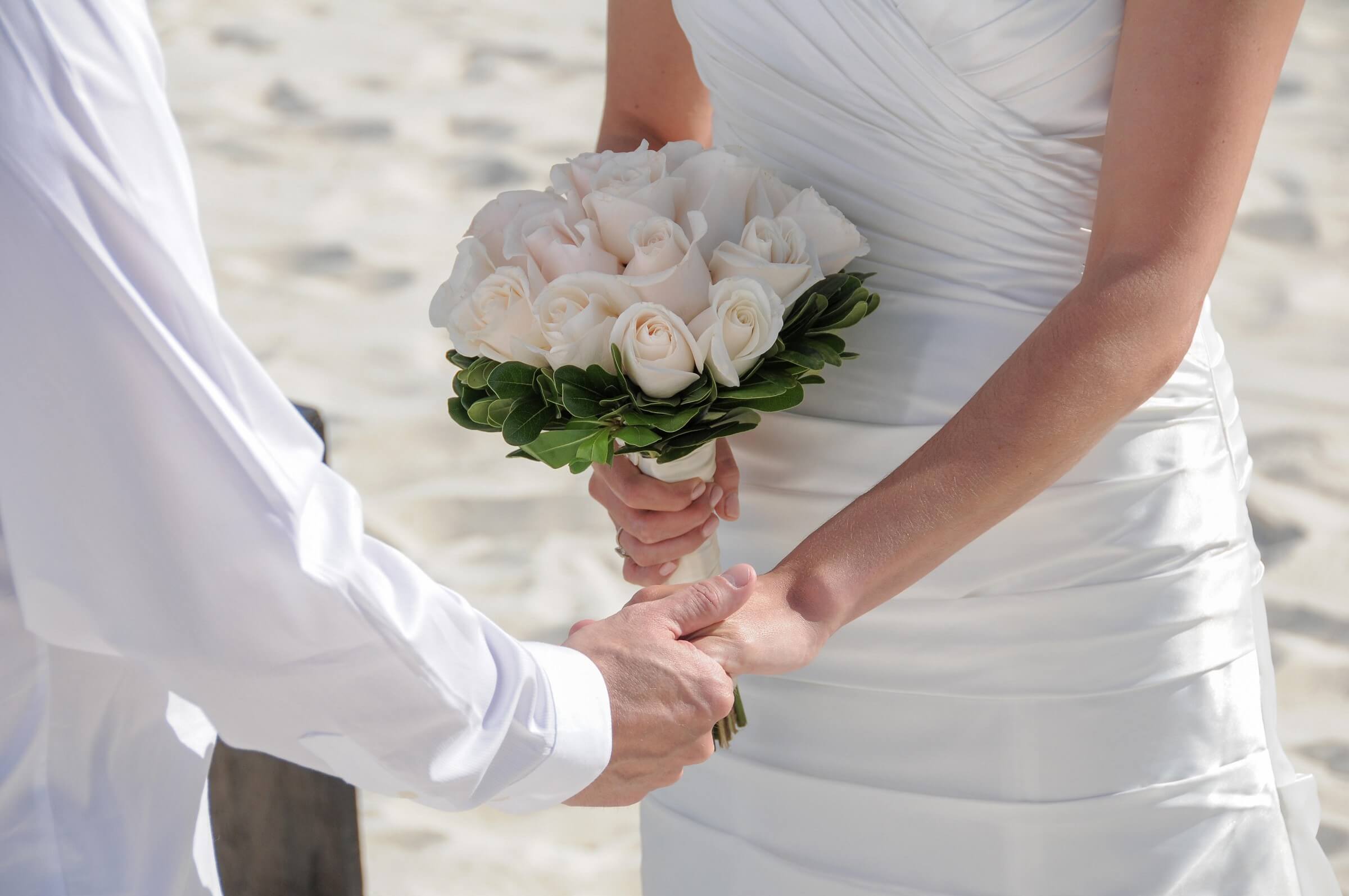 Bride and groom holding hands with a white rose bouquet on St. Pete Beach