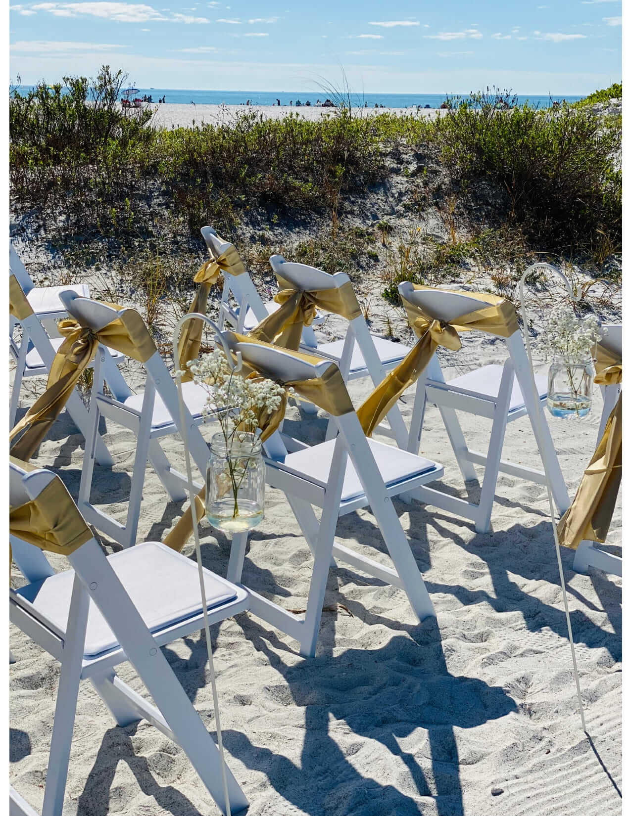 White ceremony chairs with gold sashes and baby's-breath at Sunset Beach