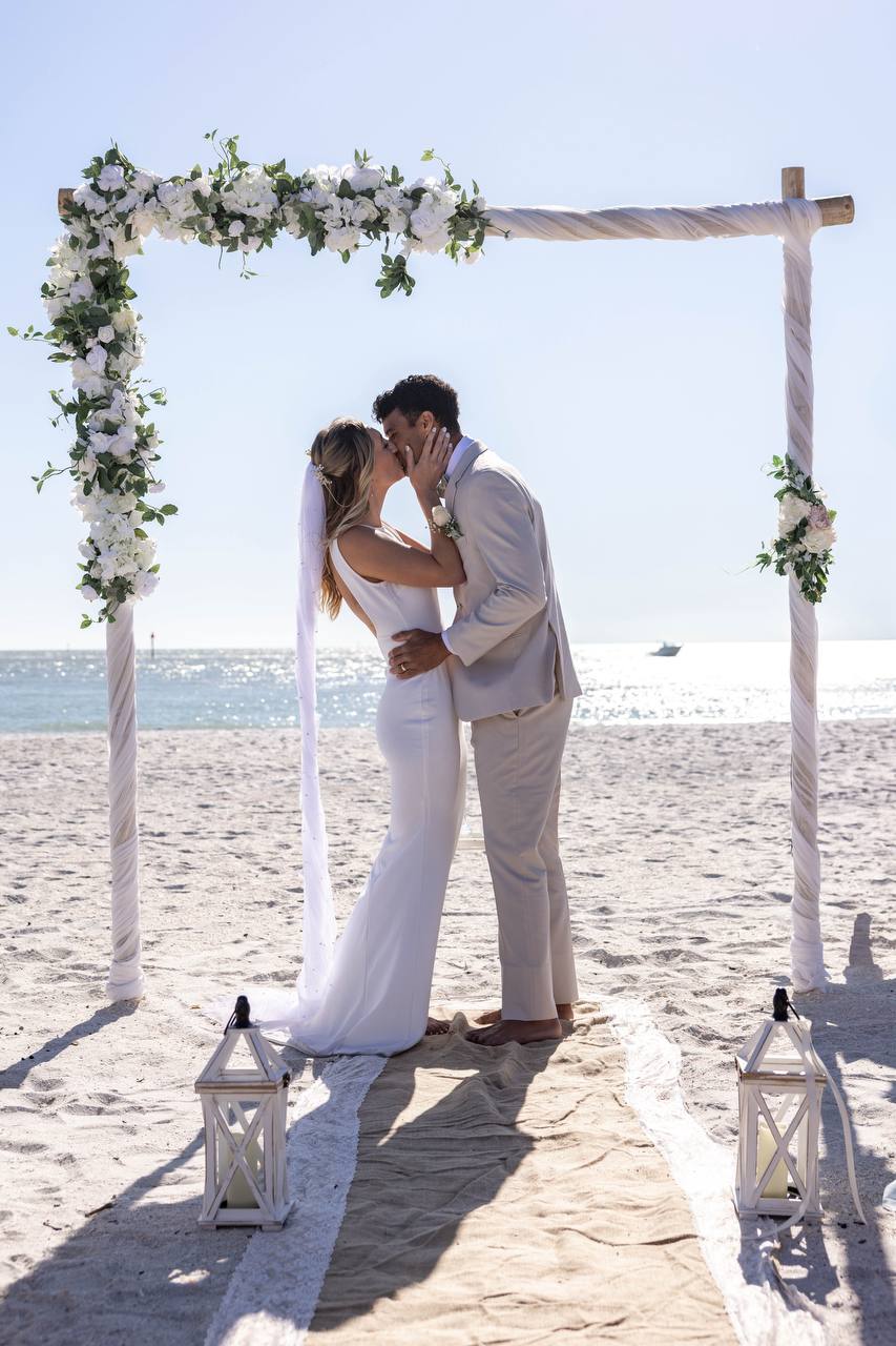 Newlyweds' first kiss under a white floral arch on Treasure Island Beach
