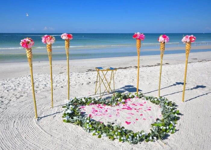 Pink rose and eucalyptus heart laid on white beach sand by the shoreline — the Simple and Pretty package