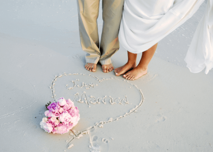 Wedding rings on a white coral dish on shell-strewn Gulf Coast sand — the You and Me elopement package